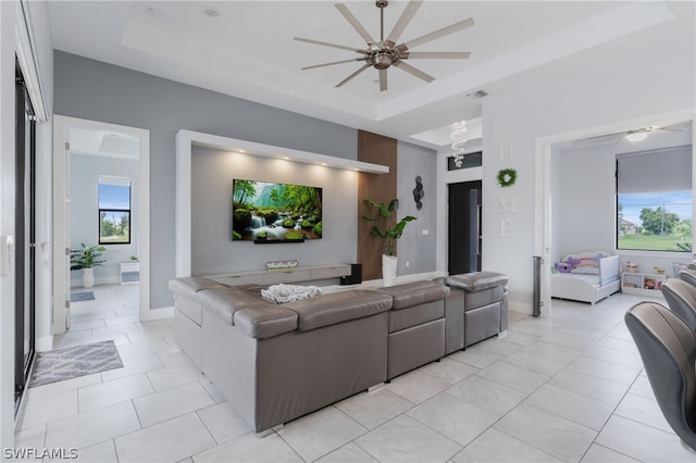 living room featuring a tray ceiling, ceiling fan, and light tile patterned floors