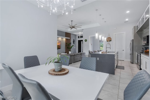 dining space with sink, ceiling fan with notable chandelier, light tile patterned floors, and a tray ceiling