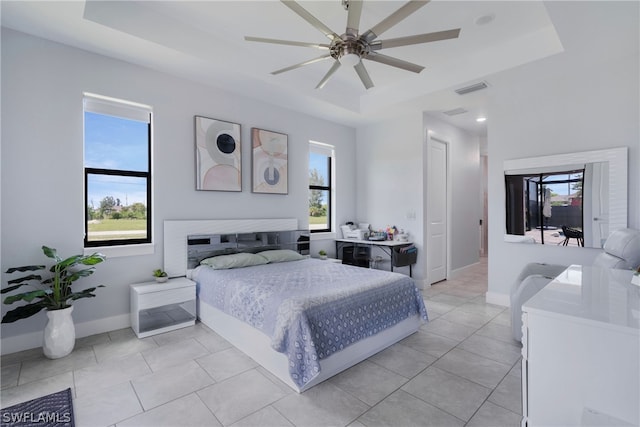 tiled bedroom with ceiling fan and a tray ceiling