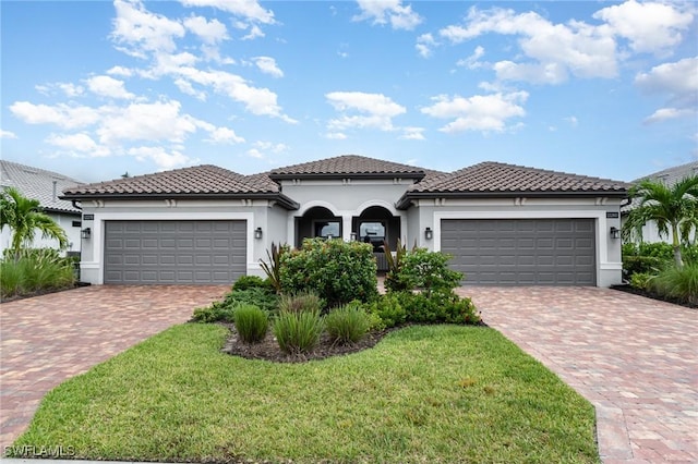 mediterranean / spanish-style home featuring decorative driveway, a tile roof, an attached garage, and stucco siding