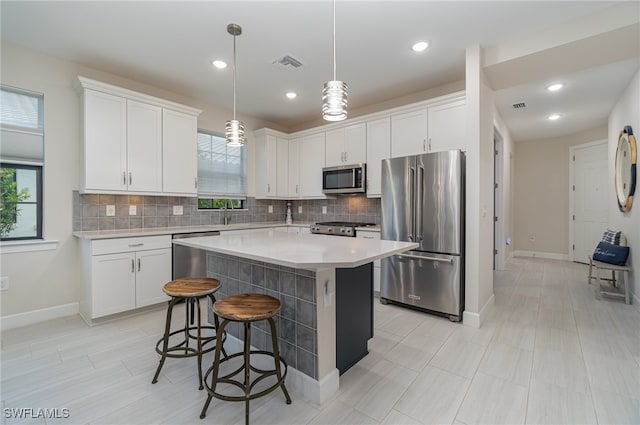 kitchen featuring decorative light fixtures, white cabinets, a center island, appliances with stainless steel finishes, and backsplash