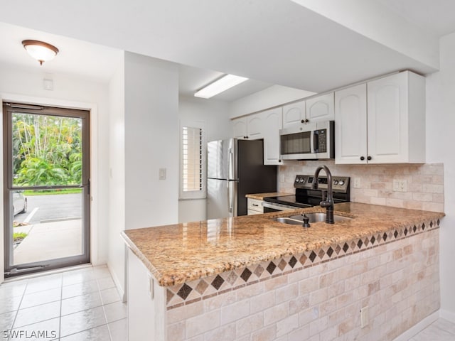 kitchen featuring appliances with stainless steel finishes, kitchen peninsula, light tile patterned floors, decorative backsplash, and white cabinetry