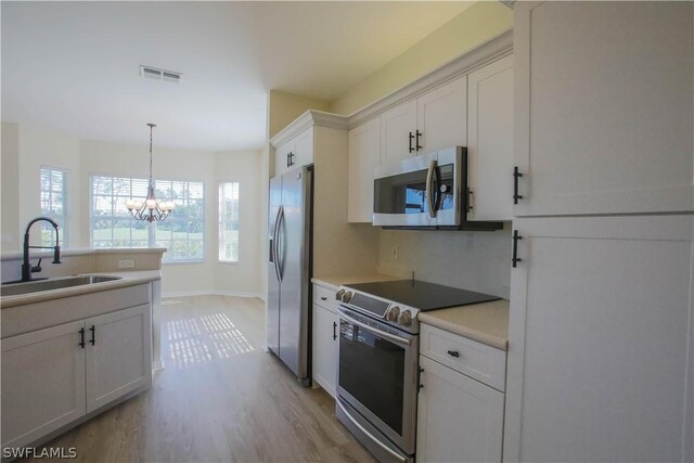 kitchen featuring white cabinetry, an inviting chandelier, stainless steel appliances, light hardwood / wood-style floors, and sink