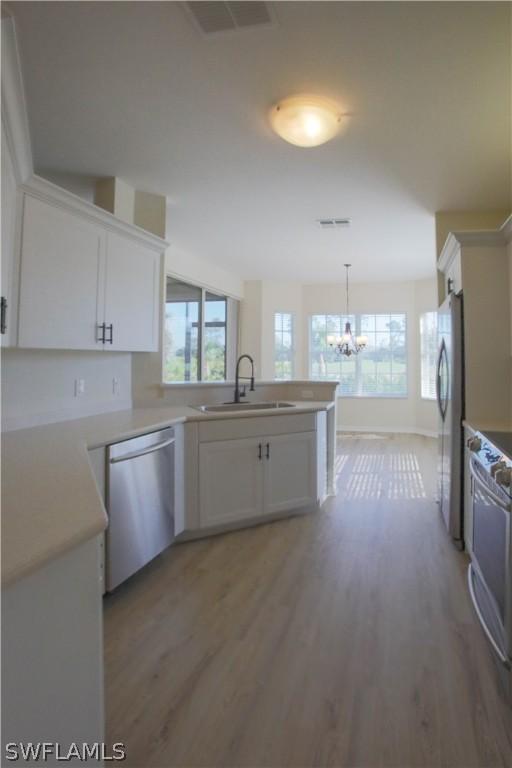 kitchen with appliances with stainless steel finishes, an inviting chandelier, wood-type flooring, and sink