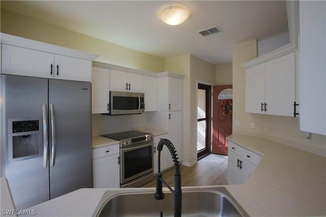 kitchen with stainless steel appliances, sink, white cabinets, and light hardwood / wood-style flooring