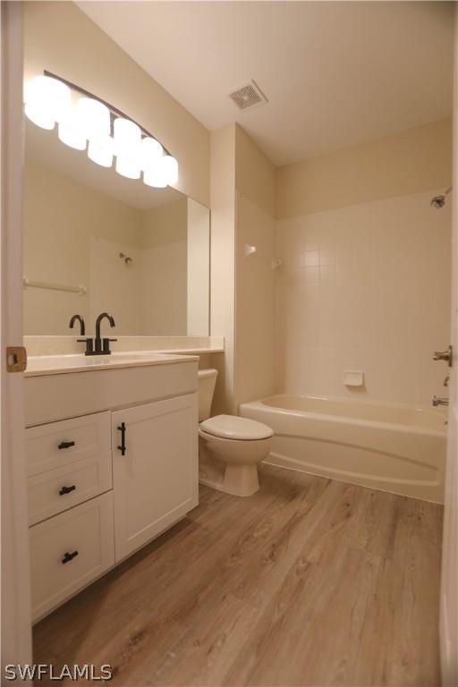 full bathroom with hardwood / wood-style flooring, vanity, tiled shower / bath combo, and toilet