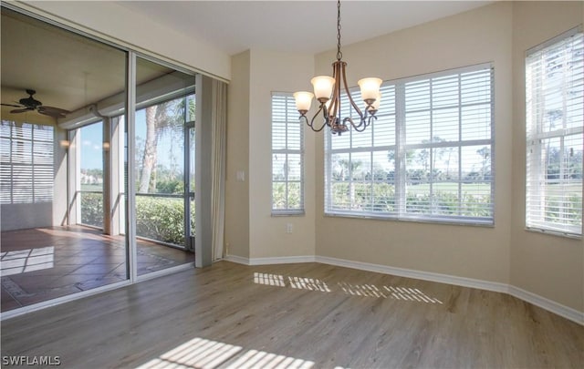 unfurnished dining area featuring ceiling fan with notable chandelier, wood-type flooring, and a healthy amount of sunlight