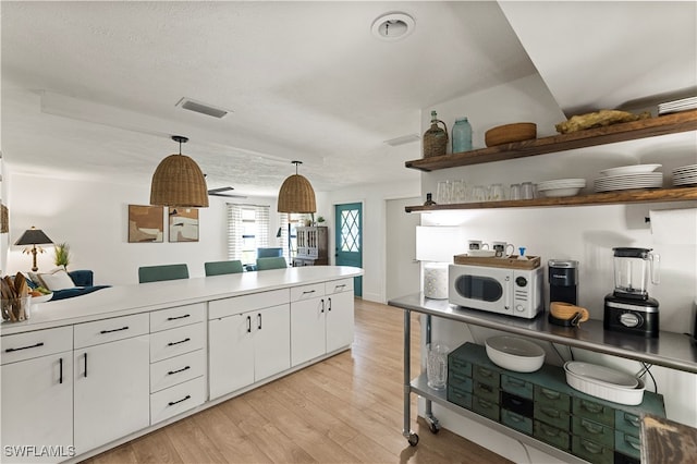 kitchen featuring white cabinets, decorative light fixtures, and light wood-type flooring