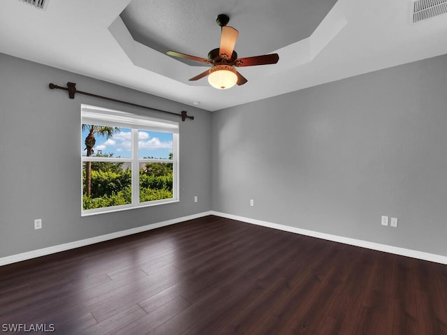 spare room with ceiling fan, dark hardwood / wood-style flooring, and a tray ceiling