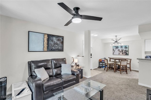 carpeted living room featuring ceiling fan with notable chandelier and baseboards