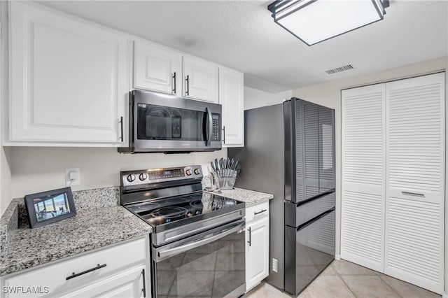 kitchen with light tile patterned flooring, white cabinetry, light stone countertops, and appliances with stainless steel finishes