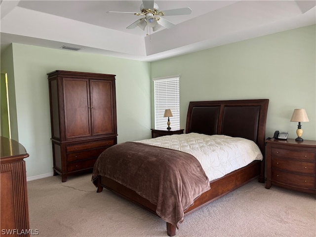 bedroom with a tray ceiling, light carpet, and ceiling fan