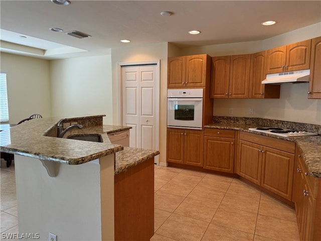 kitchen featuring white appliances, sink, dark stone countertops, a center island with sink, and light tile patterned floors