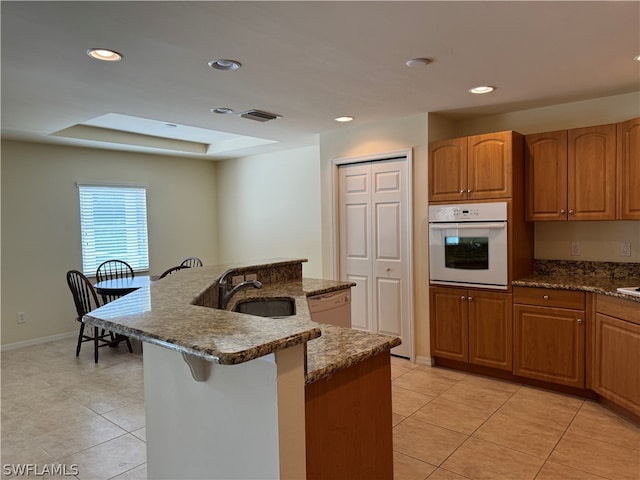 kitchen featuring white appliances, dark stone countertops, sink, light tile patterned flooring, and a raised ceiling