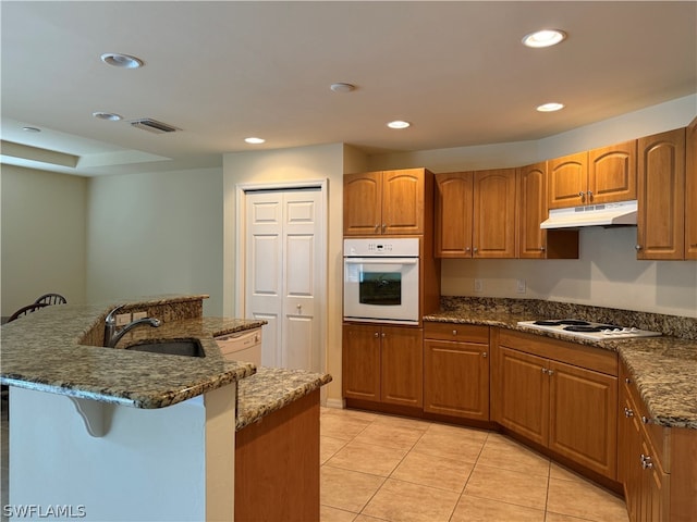 kitchen featuring sink, dark stone counters, white appliances, and light tile patterned floors