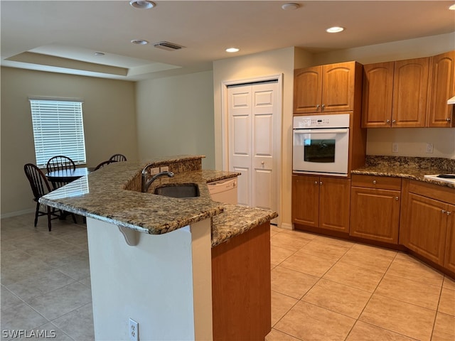 kitchen with dark stone countertops, white appliances, light tile patterned floors, a tray ceiling, and sink