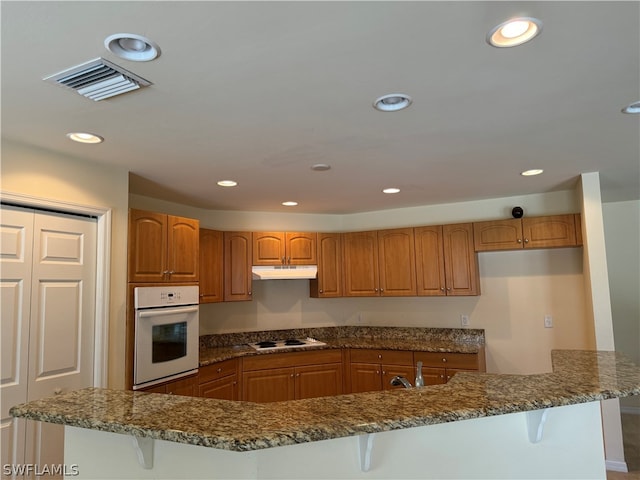 kitchen with dark stone countertops, sink, white appliances, and a breakfast bar