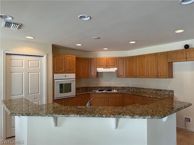 kitchen with dark stone counters, light tile patterned flooring, a breakfast bar area, and white appliances