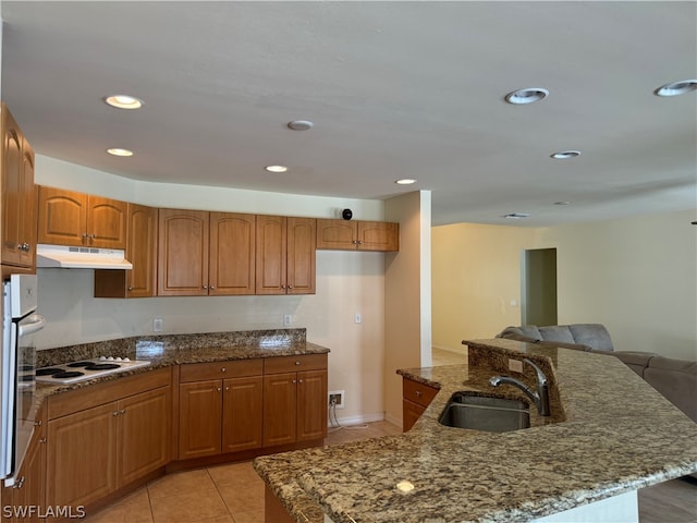 kitchen with light tile patterned flooring, dark stone countertops, white gas stovetop, oven, and sink