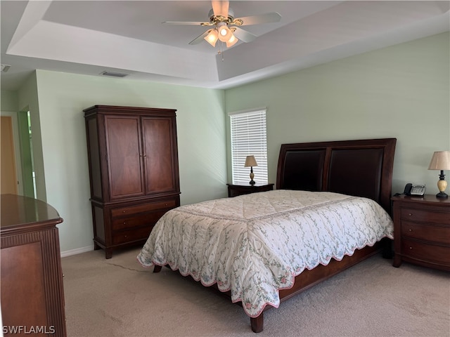 bedroom with a raised ceiling, light colored carpet, and ceiling fan