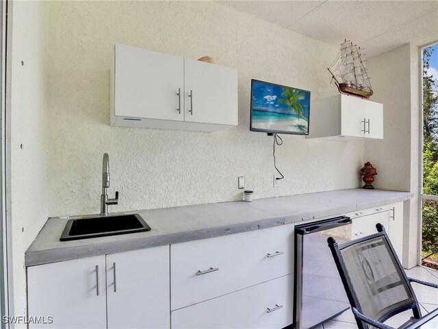 kitchen featuring stainless steel refrigerator, light tile patterned flooring, sink, and white cabinetry