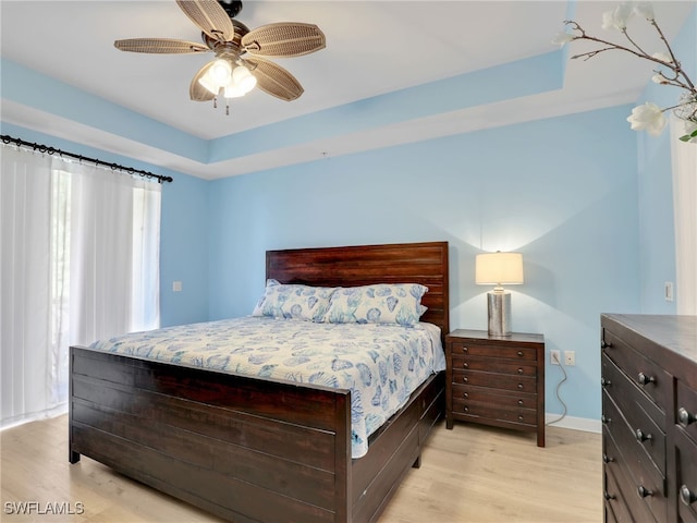 bedroom with light hardwood / wood-style floors, a raised ceiling, and ceiling fan