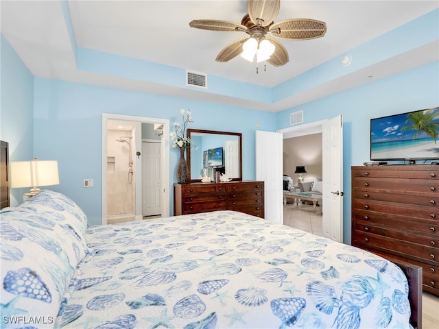 bedroom with ceiling fan, ensuite bathroom, and a tray ceiling