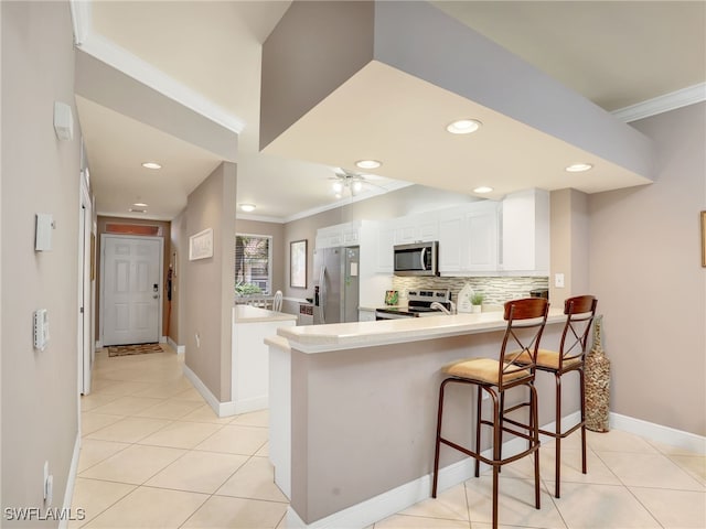 kitchen with crown molding, a breakfast bar, stainless steel appliances, white cabinets, and kitchen peninsula