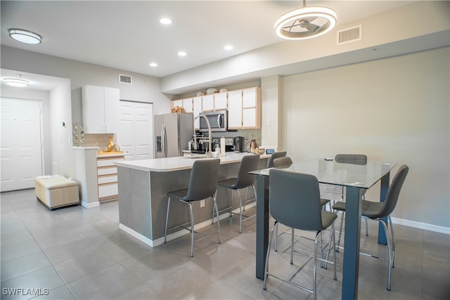 kitchen with a kitchen breakfast bar, white cabinetry, appliances with stainless steel finishes, light tile patterned floors, and kitchen peninsula