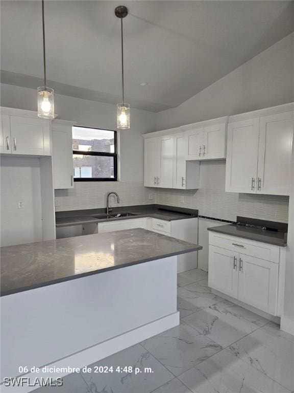 kitchen with lofted ceiling, backsplash, white cabinets, sink, and hanging light fixtures