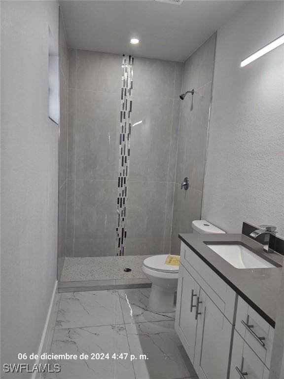 bathroom with a tile shower, vanity, and toilet