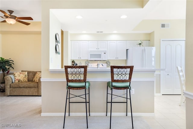 kitchen with white cabinets, a kitchen breakfast bar, white appliances, and ceiling fan