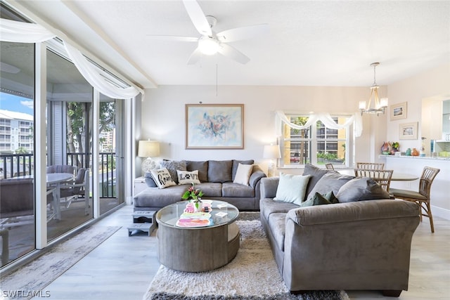 living room featuring ceiling fan with notable chandelier and light hardwood / wood-style flooring