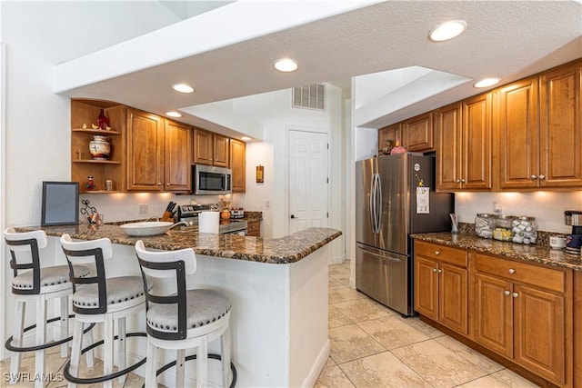 kitchen with dark stone countertops, a kitchen breakfast bar, kitchen peninsula, and appliances with stainless steel finishes