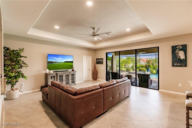 living room featuring light tile patterned flooring, ceiling fan, and a tray ceiling