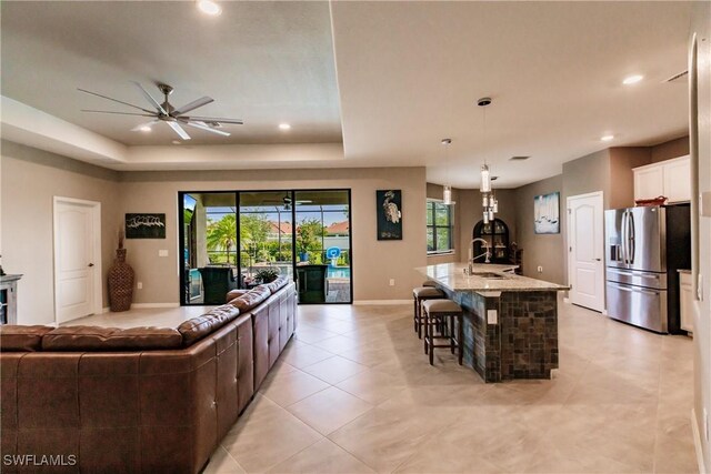 tiled living room with sink, a wood stove, ceiling fan, and a tray ceiling