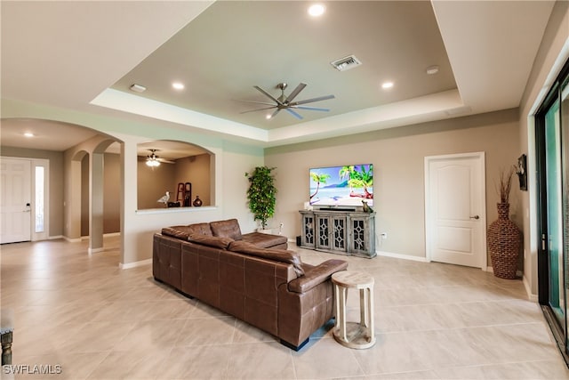 living room with light tile patterned floors, ceiling fan, and a raised ceiling