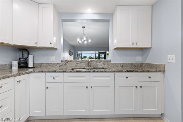 kitchen featuring pendant lighting, sink, white cabinets, dark stone counters, and an inviting chandelier