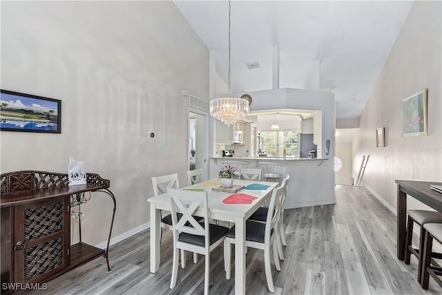 dining area featuring a notable chandelier, high vaulted ceiling, and light hardwood / wood-style flooring