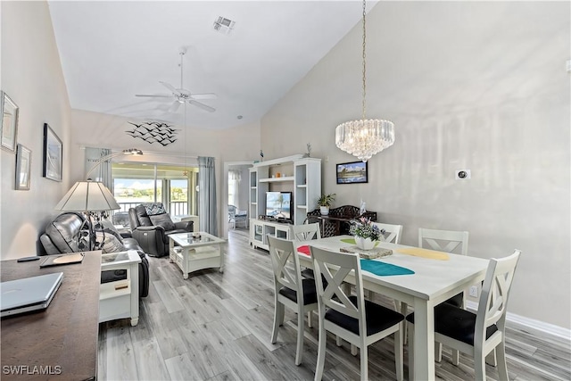 dining room with light wood-type flooring, ceiling fan with notable chandelier, and high vaulted ceiling