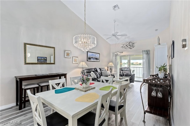 dining space featuring ceiling fan with notable chandelier, light hardwood / wood-style flooring, and high vaulted ceiling