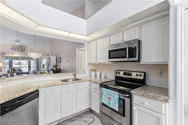 kitchen with sink, appliances with stainless steel finishes, kitchen peninsula, white cabinets, and backsplash