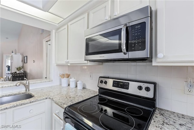 kitchen featuring sink, white cabinetry, light stone counters, stainless steel appliances, and decorative backsplash