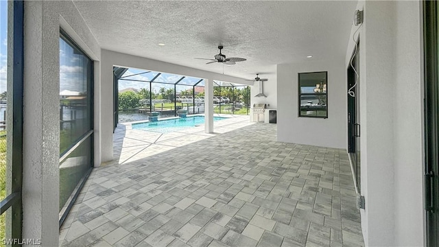 view of swimming pool featuring an outdoor kitchen, grilling area, ceiling fan, glass enclosure, and a patio area