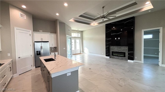 kitchen with a tray ceiling, white cabinetry, an island with sink, sink, and stainless steel fridge with ice dispenser