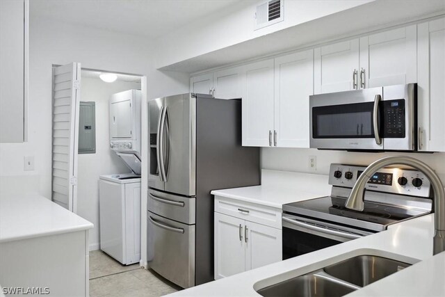 kitchen with light tile patterned floors, stainless steel appliances, stacked washing maching and dryer, and white cabinets