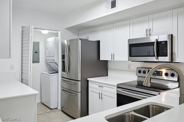 kitchen with white cabinetry, stacked washer / drying machine, stainless steel appliances, and electric panel