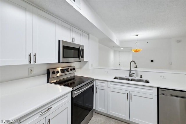 kitchen with sink, appliances with stainless steel finishes, kitchen peninsula, pendant lighting, and white cabinets