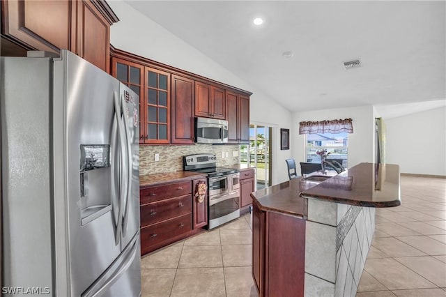 kitchen with a kitchen island, light tile patterned flooring, vaulted ceiling, and appliances with stainless steel finishes