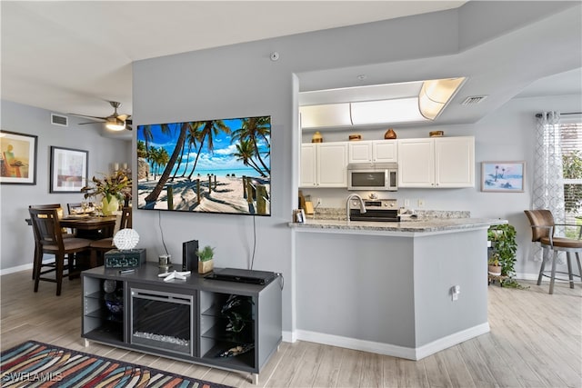 kitchen with white cabinetry, ceiling fan, stainless steel appliances, light stone counters, and light wood-type flooring